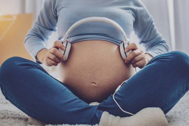 Close up of pregnant woman that holding headphones - Fotografie, Obrázek