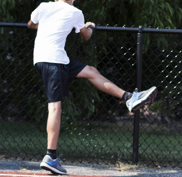 Um menino do ensino médio fazendo balanços nas pernas para se preparar para o seu treino durante o verão ao ar livre
,  - Foto, Imagem