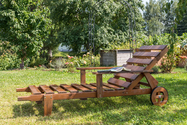 Chaise longue en bois durable dans le jardin romantique avec un livre
 - Photo, image