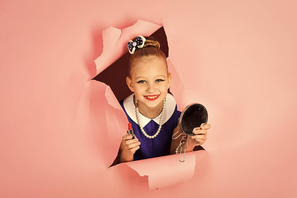 Fashion and beauty in pinup style, childhood. Retro girl, fashion, cosmetics, beauty. Makeup and retro look, hairdresser. Child girl in stylish dress, makeup. Little girl hold lipstick and mirror. - Photo, Image