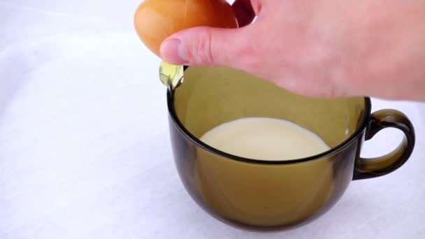 Lidská ruka láme syrové vejce do misky mléka ve zpomaleném filmu. - Záběry, video