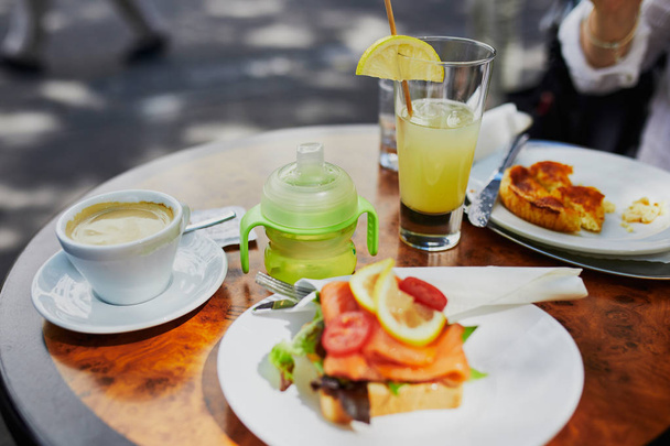 Cup of coffee, glass of juice, snacks and baby drinking bottle on the table of cafe or restaurant. Eating out with children - Photo, image
