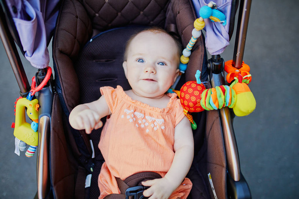 Baby girl with colorful toys in stroller. Little child in pram. Infant kid outdoors - 写真・画像