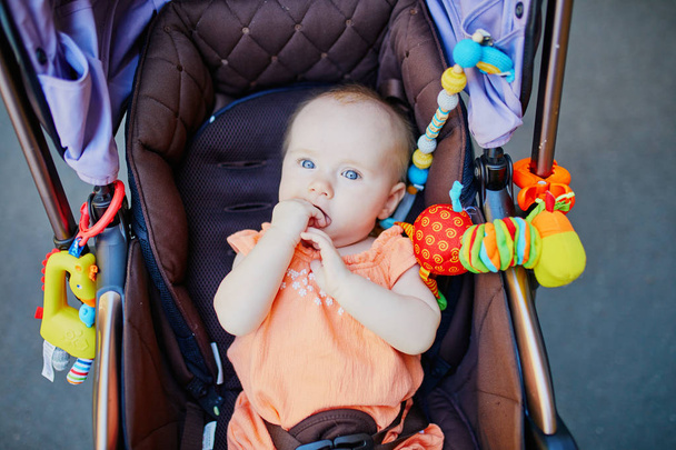 Baby girl with colorful toys in stroller. Little child in pram. Infant kid outdoors - Фото, зображення