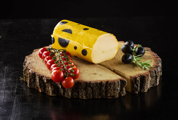 Piece of Salami cheese, cherry tomatoes and olives on wooden board over black - Fotografie, Obrázek