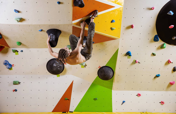 Young man climbing challenging bouldering route. In indoor climbing gym. - Photo, Image