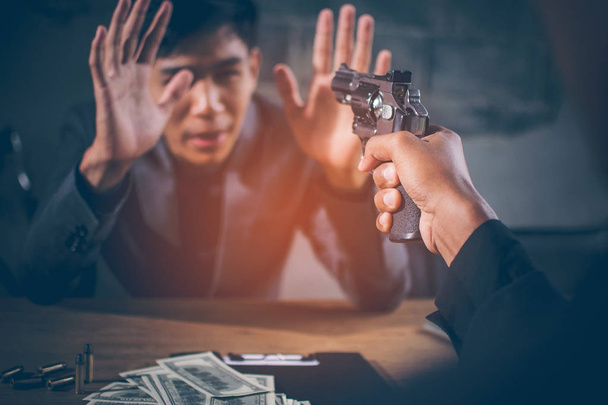 Kriminelle haben es auf junge Geschäftsleute abgesehen. Dollarnoten usd und Kugeln auf dem Tisch, der junge Mann Hand zeigen Anzeichen der Kapitulation und sieht verängstigt, Konzept Erpressung, Erpressung von Unternehmen. - Foto, Bild
