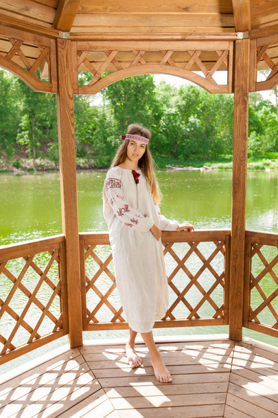 湖畔に木製の夏 altanka の刺繍に身を包んだ美しいウクライナの女性 - 写真・画像