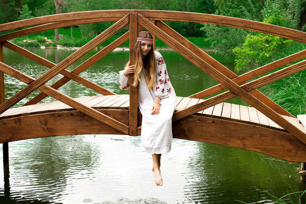 Belle femme ukrainienne portant une broderie se trouve sur un pont en bois sur un étang
 - Photo, image