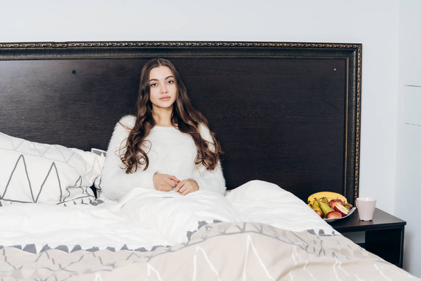 sleepy young girl in white pajamas resting in bed in the evening, wants to sleep - Fotografie, Obrázek