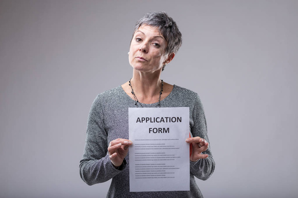Mujer mayor embarazada sosteniendo un formulario de solicitud mecanografiado con una expresión superior sobre gris con espacio de copia
 - Foto, imagen