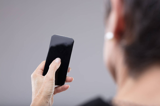 Woman holding a blank mobile phone in her hand in an over the shoulder view of her thumb on the screen - Foto, Imagen