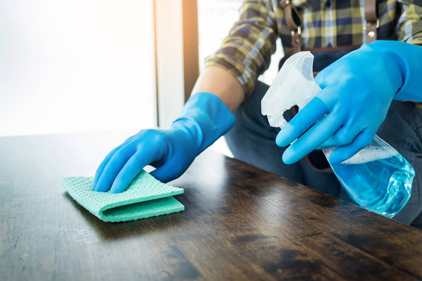 man with cloth cleaning wooden table in home uses rag and fluid in a spray - Photo, Image