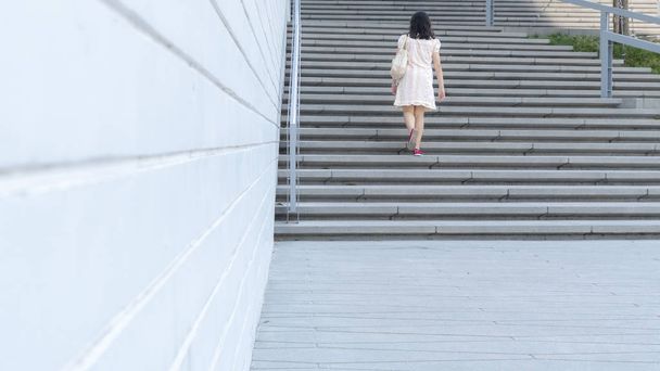 girl is walking up the exterior concrete stair with landscape city background - Foto, Imagen