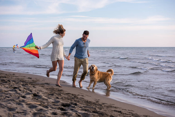 Young Couple having fun playing with a dog and Kite on the beach at autumn day - Foto, Bild