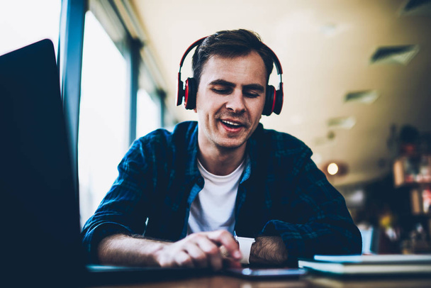 Good looking smiling male student listening to funny music and searching new compositions on smartphone connected to 4G.Young positive man enjoying resting in coffee shop with headphones and device - Photo, image
