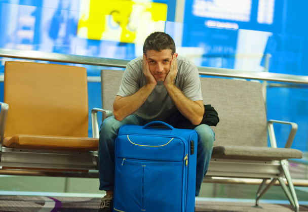 lifestyle portrait of young happy and attractive tourist man sitting with suitcase at airport departure boarding gate waiting relaxed and cheerful for flight in tourism trip and holidays travel  - Foto, Imagen
