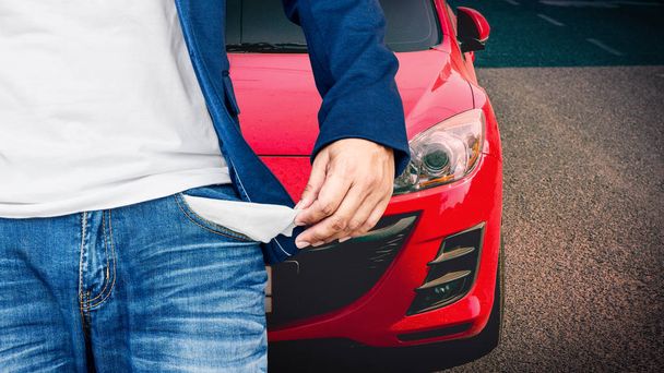 Man showing his empty pocket with red car parked on the street. - Фото, изображение