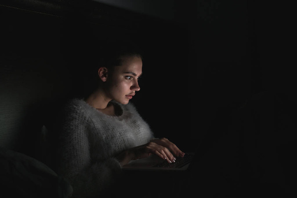 sleepy young girl sitting in bed late at night watching a movie on her laptop - Foto, imagen