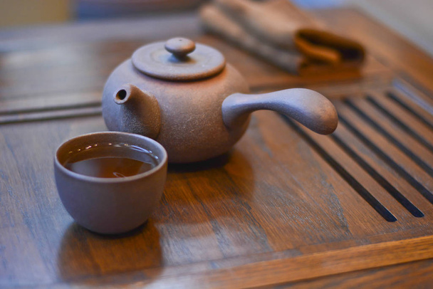 Chinese tea service for tea: wooden stand, clay cup with a tea and teapot with a handle close-up - 写真・画像