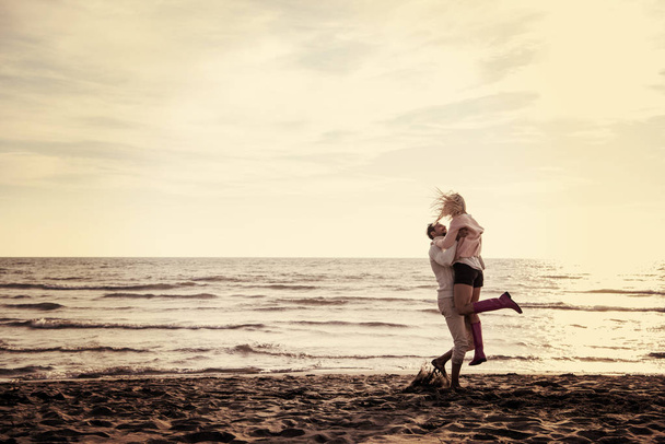Young couple having fun walking and hugging on beach during autumn sunny day filter - Foto, imagen