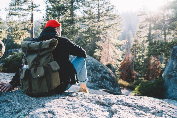 Back view of male explorer with touristic backpack sitting on rock enjoying beautiful scenery of forest landscape, guy wanderlust on hiking tour in Yosemite national park during active weekend - Foto, Imagem