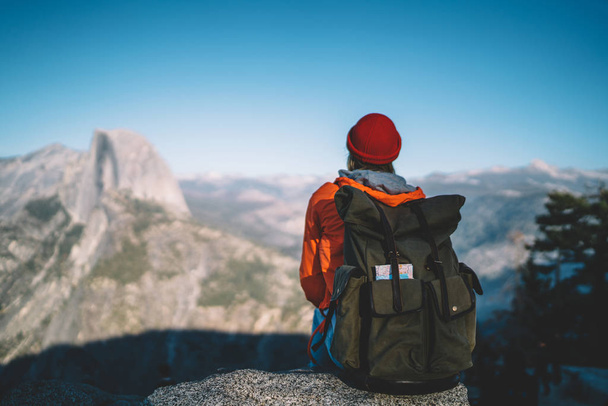 Back view of female hiker with rucksack sitting on viewpoint resting during tour enjoying breathtaking landscape of high rock hills,girl wanderlust recreating observe natural scenery from viewpoin - Photo, Image
