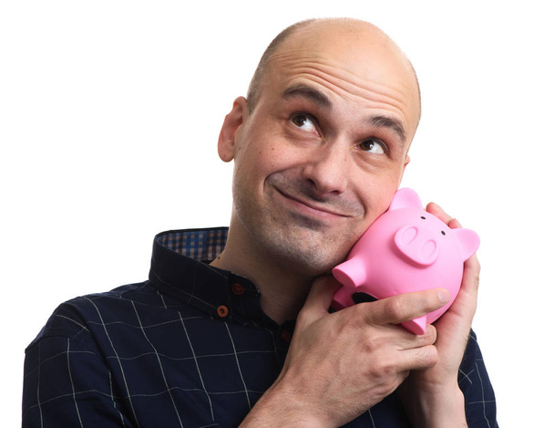 Ein glücklicher Glatzkopf hält ein Sparschwein in der Hand. fröhlicher Typ, der vom Geld träumt. isoliert - Foto, Bild