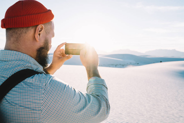 Back view of male traveler with smartphone taking picture of beautiful desert landscape, cropped image of guy wanderlust making photo of dunes on modern cellular camera exploring White sands - Foto, Bild