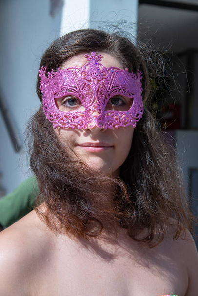Cara de hermosa chica morena con máscara de carnaval de color púrpura con signos en relieve. Mira en la cámara. Sombreros movidos en el cuello
. - Foto, imagen