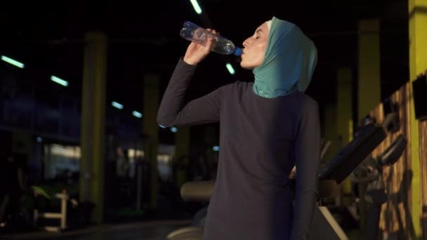 Young sporty muslim girl in hijab drinking water from bottle after workout - Кадры, видео