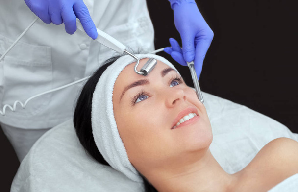 Kosmetolog sprawia, że aparatura jest zabiegiem terapii mikroprądowej pięknej, młodej kobiety w salonie piękności. Kosmetologia i profesjonalna pielęgnacja skóry. - Zdjęcie, obraz
