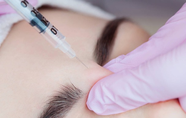 The doctor cosmetologist makes the Botulinum Toxin injection procedure for tightening and smoothing wrinkles on the face skin of a beautiful, young woman in a beauty salon.Cosmetology skin care. - Valokuva, kuva