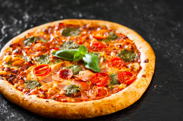 Pizza with Mozzarella cheese, Ham, Tomatoes, pepper, Spices and Fresh Basil pesto sauce. Italian pizza.on black background. - Fotó, kép
