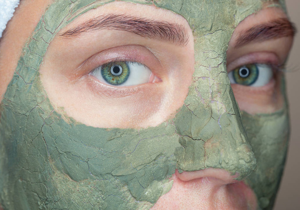 Η διαδικασία για την εφαρμογή μιας μάσκας από πηλό στο πρόσωπο μιας όμορφης γυναίκας. Spa θεραπείες και φροντίδα των γατών στο σαλόνι ομορφιάς. - Φωτογραφία, εικόνα