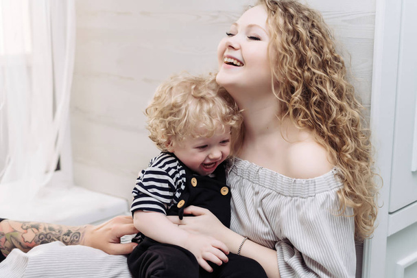 friendly family, beautiful curly mother playing with her little son, hugging and laughing - Fotó, kép