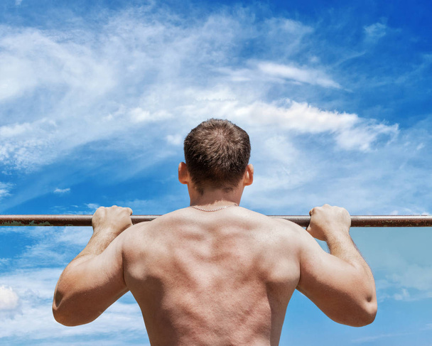 Strong athlete doing pull-up on horizontal bar. Closeup view. Mans fitness at the blue sky background. - Photo, Image