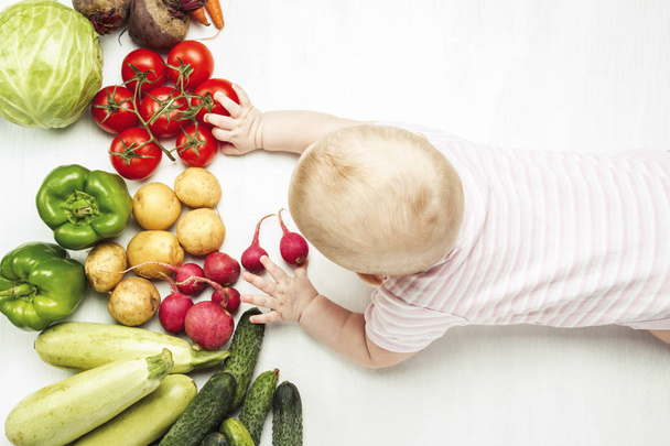 Little baby reach a hand to fresh organic vegetables on a light wooden background. Care for health. Healthy baby food. Flat lay, top view. - Foto, Imagem