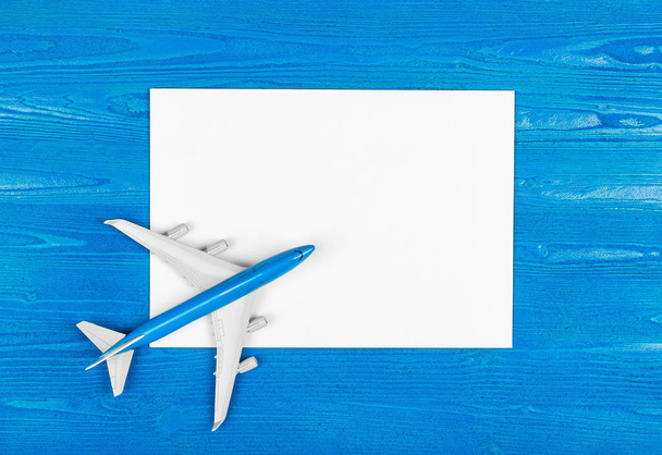 Μοντέλο του αεροπλάνου και κενό φύλλο χαρτιού στο μπλε φόντο ξύλινη. Έννοια του ταξιδιού. - Φωτογραφία, εικόνα
