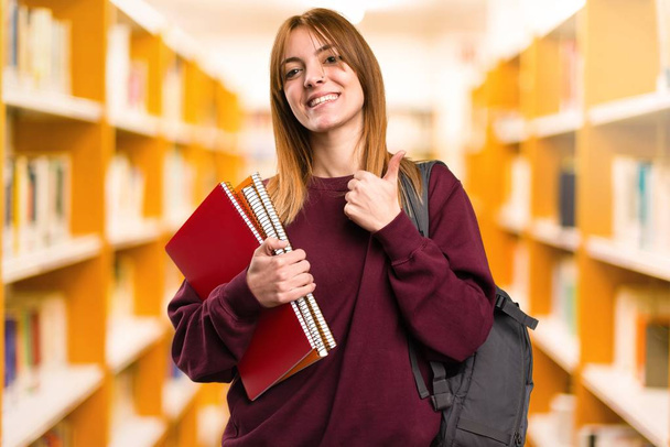 Studentin mit erhobenem Daumen auf unkonzentriertem Hintergrund - Foto, Bild