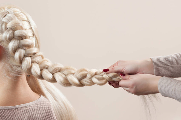 Schöne Mädchen mit blonden Haaren, Friseur webt einen Zopf Nahaufnahme, in einem Schönheitssalon. Professionelle Haarpflege und Frisurengestaltung. - Foto, Bild