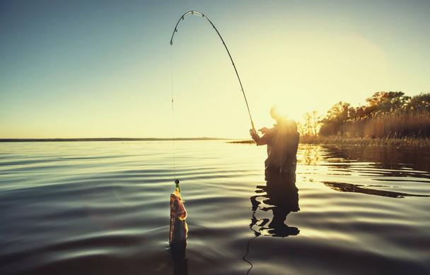 Un pêcheur avec une canne à pêche à la main et un poisson pris se tient dans l'eau
 - Photo, image