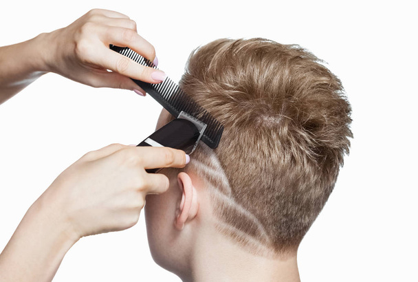 Un coiffeur fait une coupe de cheveux pour un jeune homme dans un salon de coiffure. - Photo, image