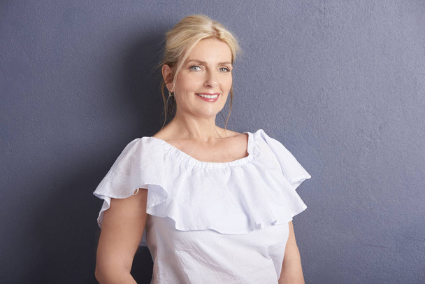 hermosa mujer sonriente madura con blusa blanca contra la pared gris
 - Foto, imagen