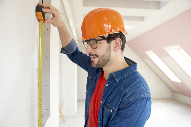 Portrait of young man using measuring tape while working on construction site.  - 写真・画像