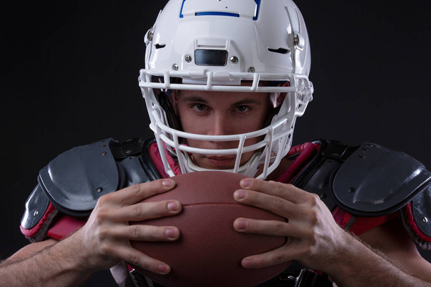ユニフォームとヘルメット ブラックに分離されたボールを保持している筋肉のアメリカン フットボール選手の低角度のビュー - 写真・画像