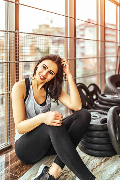 Pretty sporty woman smiling and looking at camera while sitting in gym - Valokuva, kuva