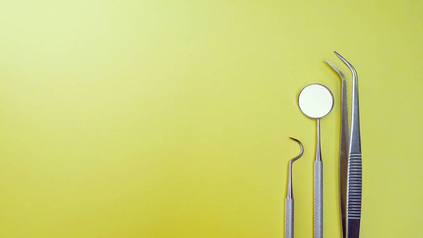 Professional dentist instruments in dental clinic. Dentist mirror, forceps curved, explorer curved, dental explorer angular and explorer curved with chip at yellow background - Photo, Image