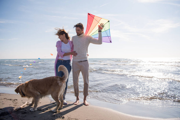 Young Couple having fun playing with a dog and Kite on the beach at autumn day - Foto, afbeelding
