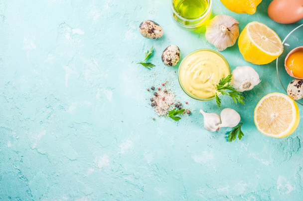 hausgemachte Mayonnaise-Sauce mit Zutaten - Zitrone, Eier, Olivenöl, Gewürze und Kräuter, hellblauer Hintergrund Kopierfläche oben - Foto, Bild
